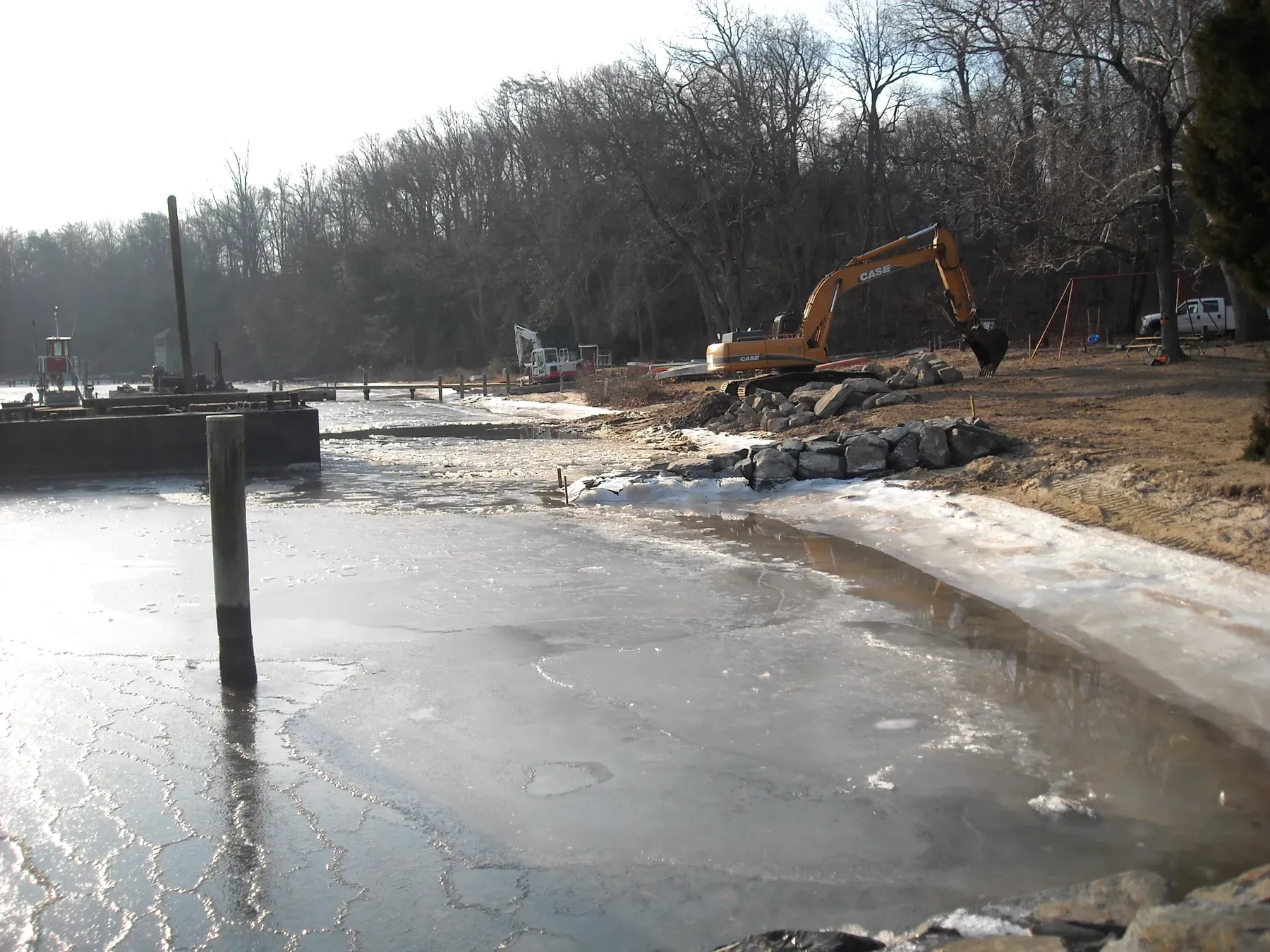 Excavator working a shoreline with ice on the water